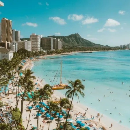 Aerial view of Waikiki Beach in Honolulu, Hawaii, featuring turquoise waters, golden sand, and high-rise hotels with Diamond Head crater in the background.