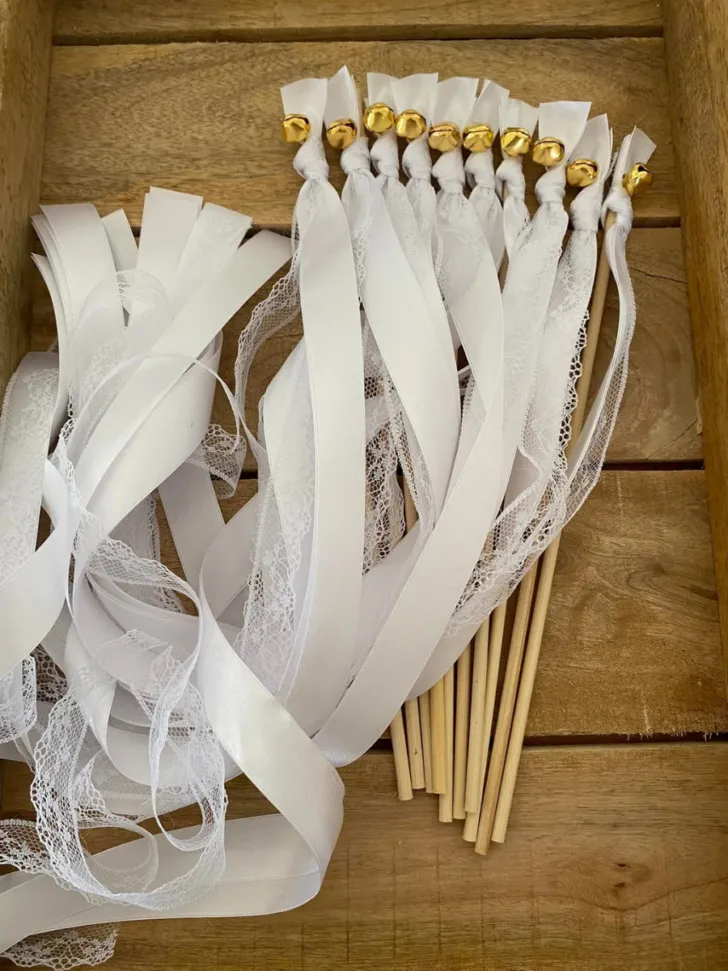 Luxurious white wedding ribbon wands with a mix of satin and lace ribbons, topped with golden bells, beautifully arranged in a wooden crate, ready to enhance the celebratory mood of a wedding send-off.