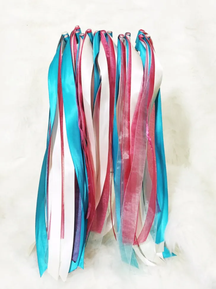 A collection of vibrant wedding ribbon wands in turquoise, pink, and white, clustered together and displayed on a fluffy white background, ideal for adding a splash of color to any wedding celebration.