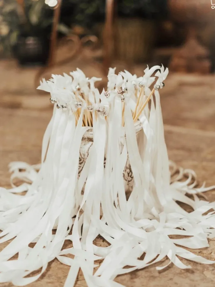 Elegant white wedding ribbon wands with long, flowing ribbons and crystal embellishments, beautifully displayed in a rustic vase, ready for a sophisticated ceremony or reception send-off.