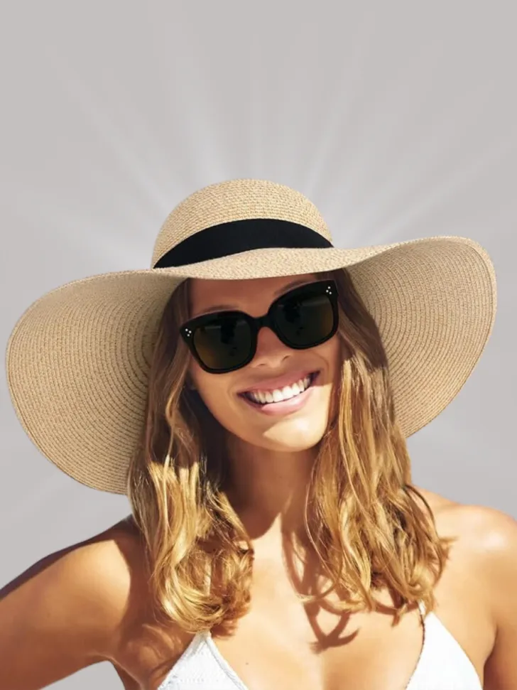 A woman smiling in a large sun hat with a black band and wearing dark sunglasses, perfect for a sunny vacation or beach day.