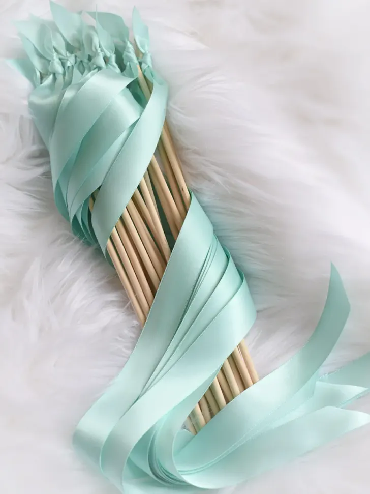 A bundle of elegant aqua-colored wedding ribbon wands neatly tied together, resting on a plush white fur background, exuding a calm and sophisticated charm ideal for a refined wedding celebration.